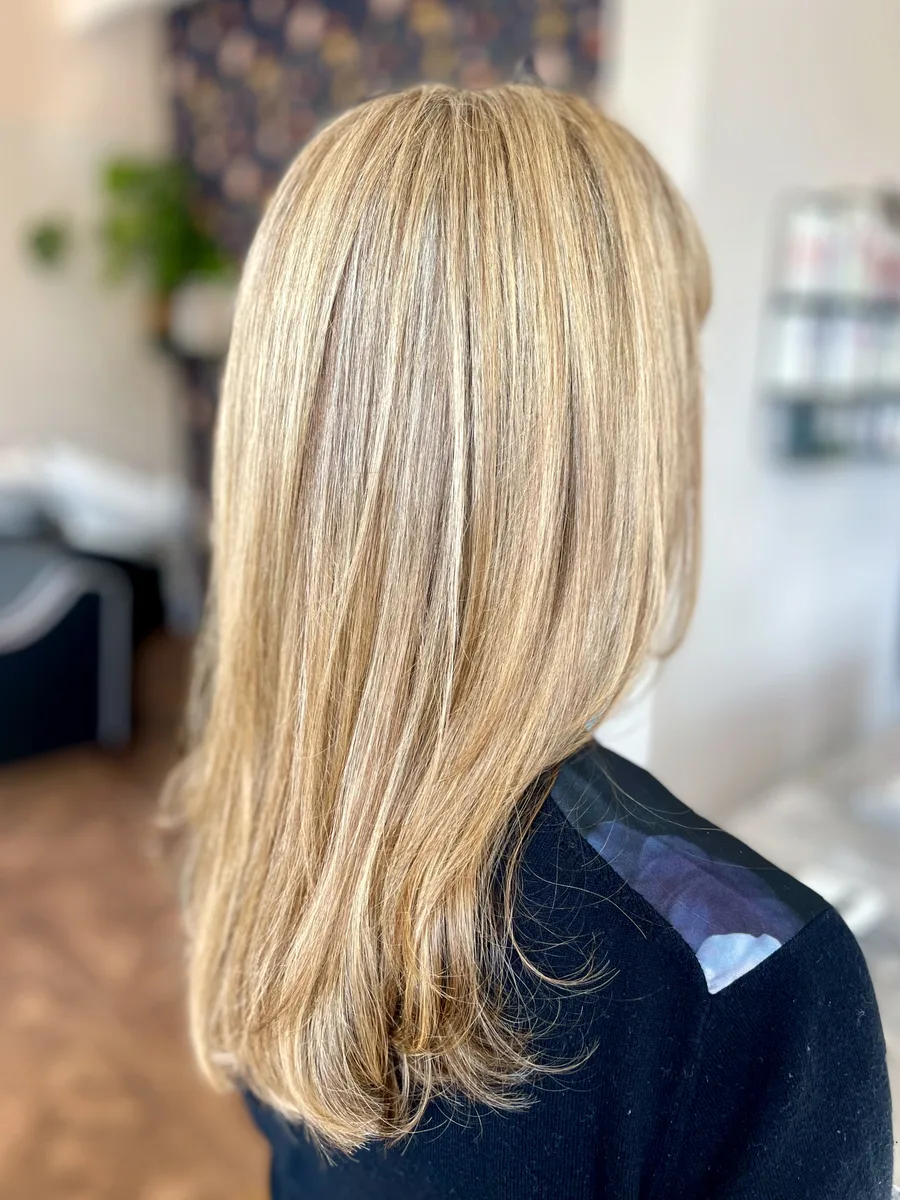 Golden blonde highlights on long, softly layered hair — warm dimensional color, side view.