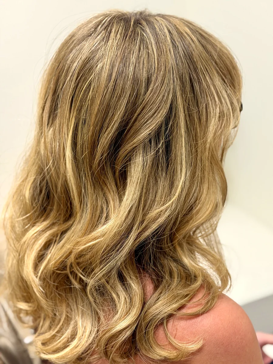 Golden blonde highlights on mid-length layers, styled in loose waves — side view.