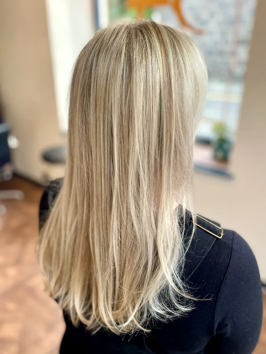 Creamy blonde highlights on long, straight hair — soft dimensional color, back view.