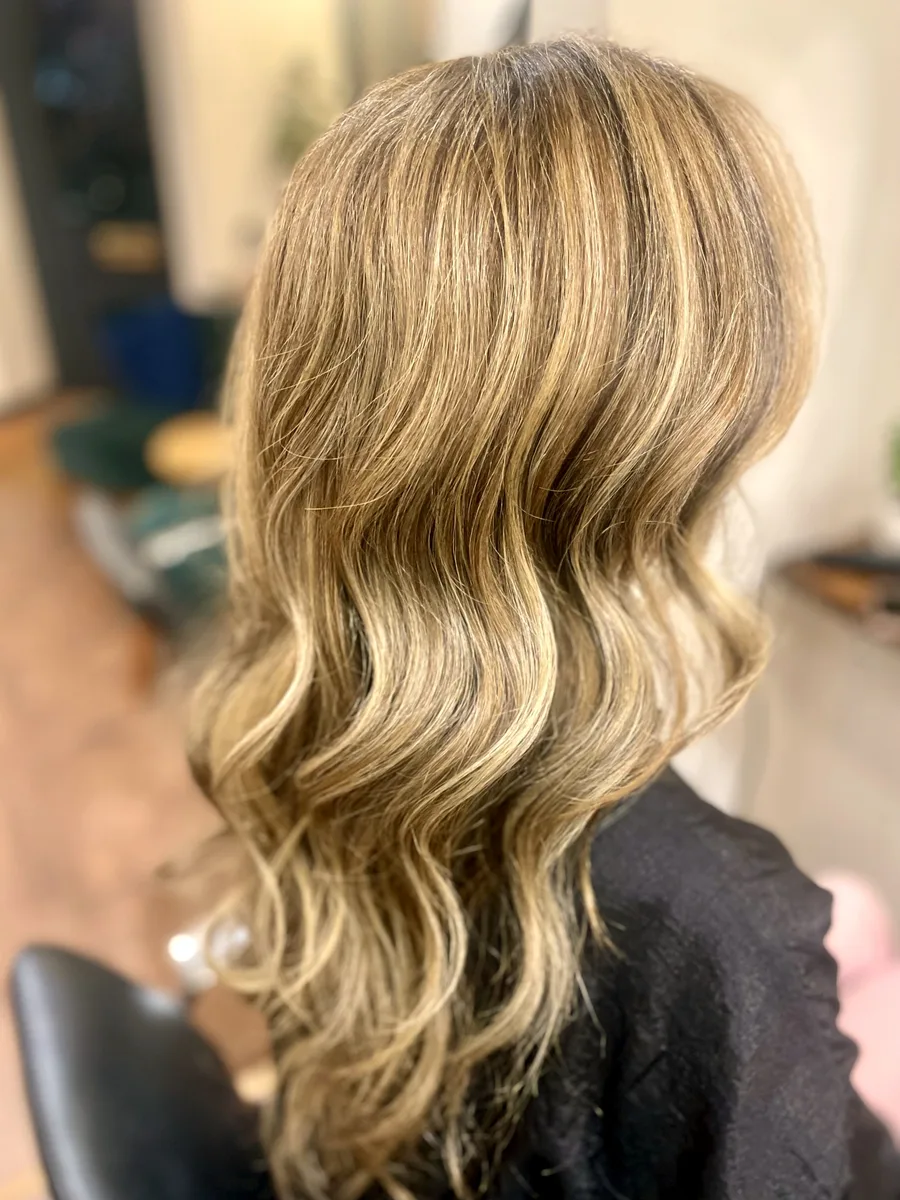 Soft, dimensional blonde highlights on long layered hair, finished in loose waves.