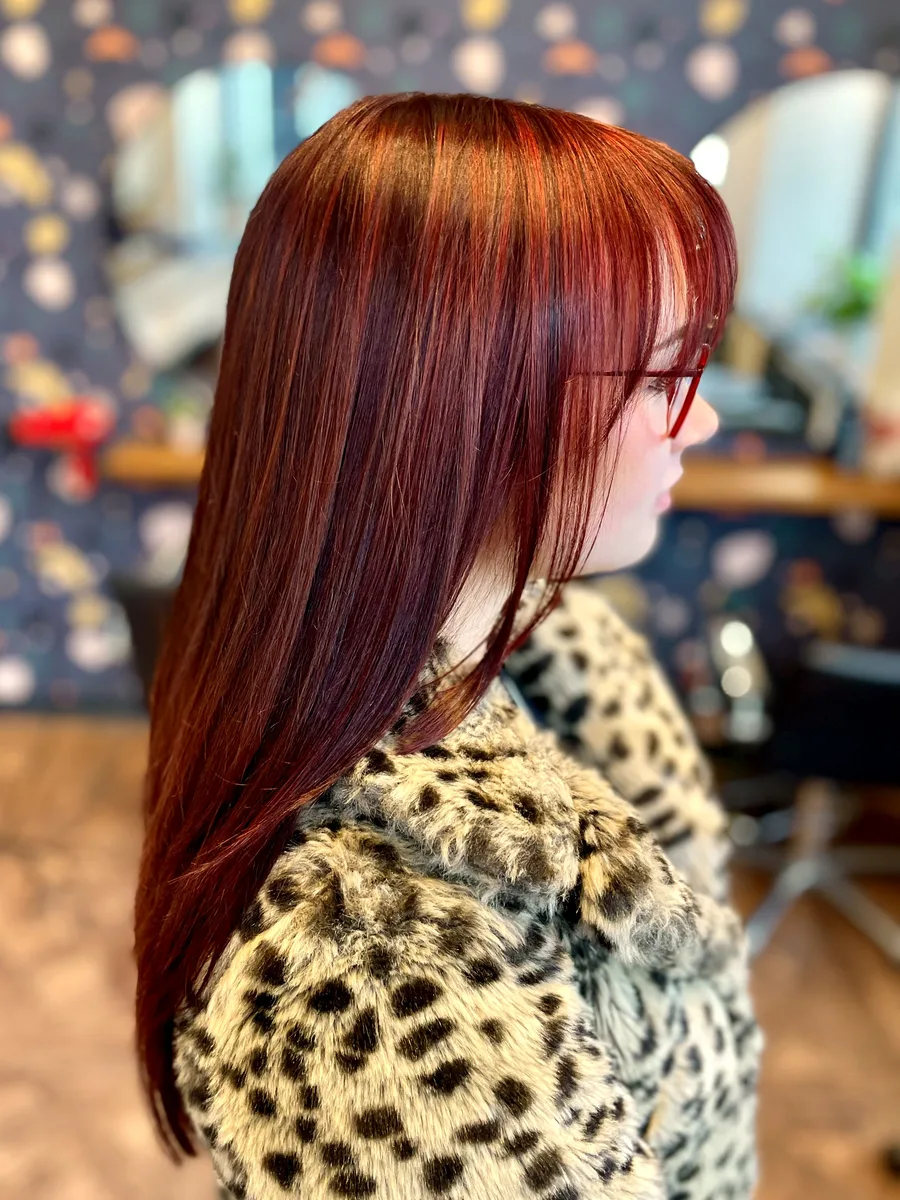Vivid copper-red single-process color with face-framing bangs, styled straight — side profile.