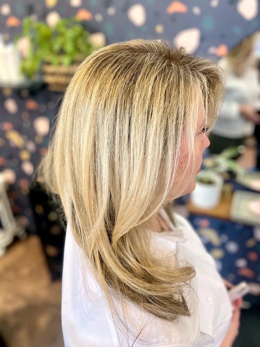 Buttery blonde highlights on long layers with a polished blowout — side view.